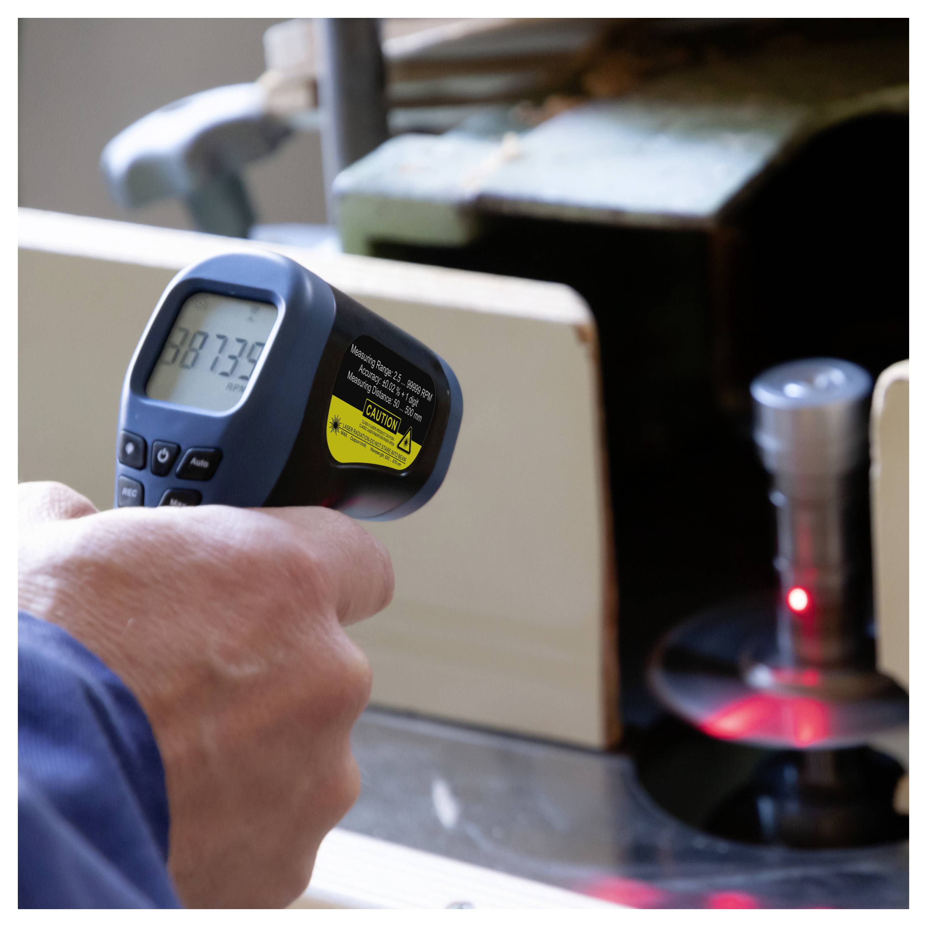 Personne utilisant un thermomètre infrarouge portatif pour mesurer la température d'une machine ou d'une surface métallique, avec un point laser rouge indiquant la zone cible.