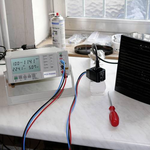 Un appareil de mesure avec des affichages numériques montre des valeurs à côté d'une prise électrique, d'un tournevis et d'une bombe aérosol sur une table.