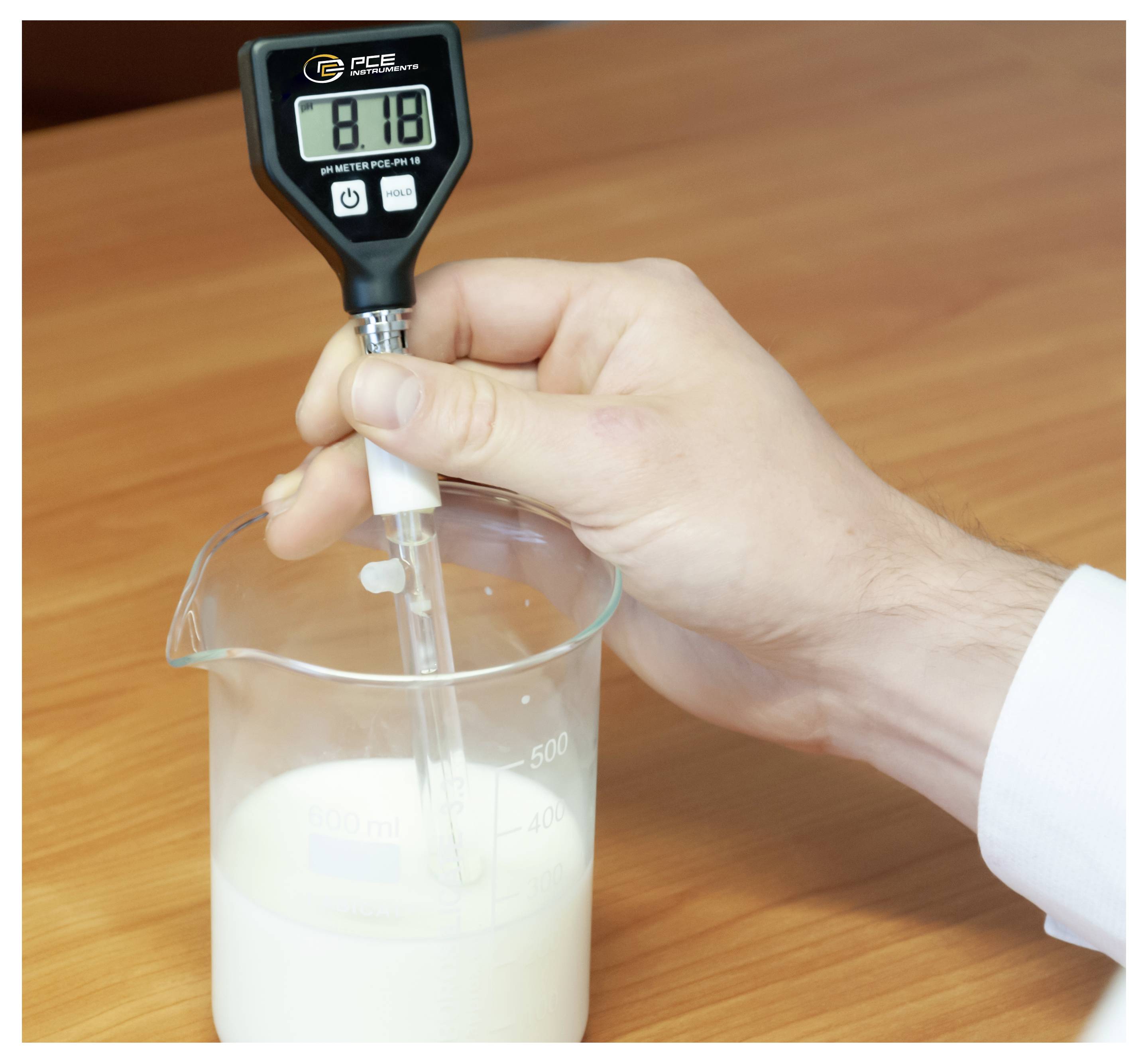 Main tenant un pH-mètre numérique dans un bécher de lait sur une table en bois, mesurant l'acidité.