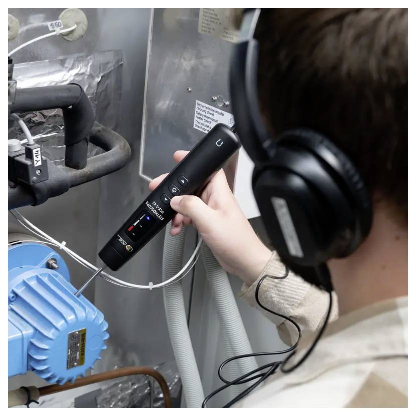 Une personne portant des écouteurs utilise un appareil portatif pour inspecter des machines dotées de composants bleus et noirs, ce qui indique une opération technique.