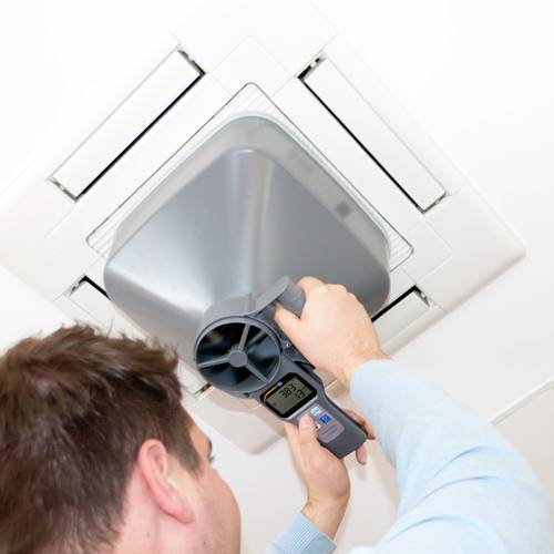 Un homme règle l'unité de ventilation dans le plafond à l'aide d'un appareil de mesure. L'affichage indique la température. Installation de poste de travail.