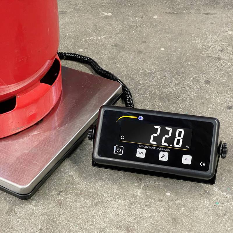 Bouteille de gaz rouge posée sur une balance numérique, affichant 22,8 kg. La balance et la bouteille sont placées sur un sol gris.