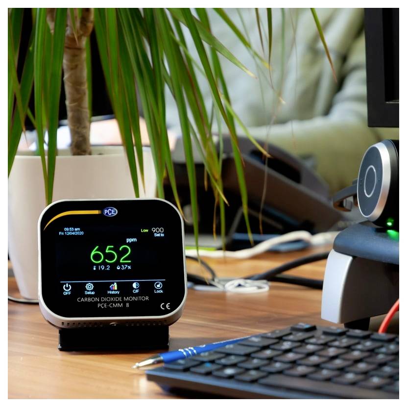 Moniteur numérique de CO2 sur un bureau affichant 652 ppm, avec un clavier, un stylo, une plante et du matériel de bureau en arrière-plan.