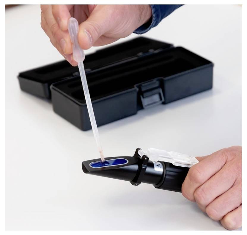 Une personne utilisant une pipette pour verser du liquide dans un appareil de test sanguin portable à côté d'une mallette de transport ouverte.