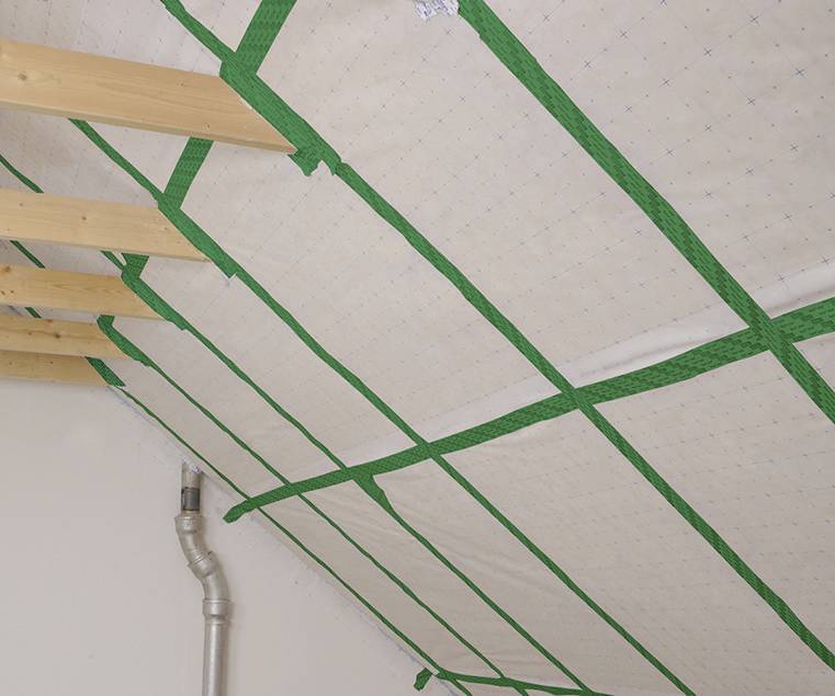 Une construction de toiture avec des poutres en bois apparentes et un pare-vapeur vert fixé diagonalement sur le plafond.