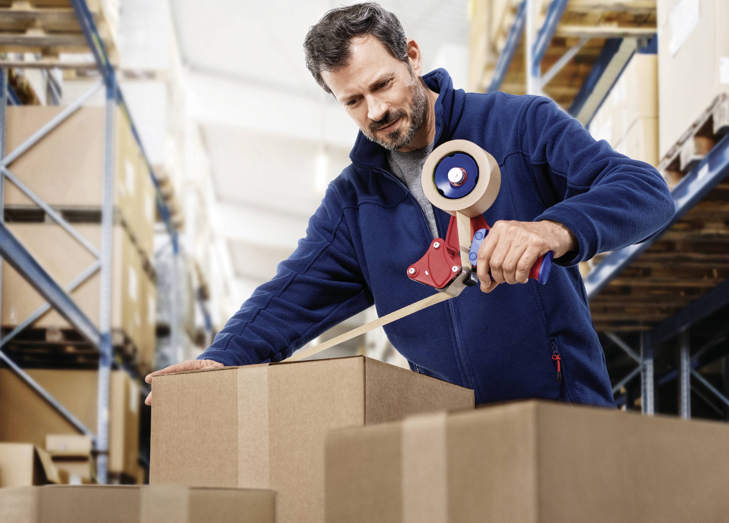 Homme dans un entrepôt, fermant un carton avec du ruban adhésif. Des étagères remplies de cartons sont visibles en arrière-plan.