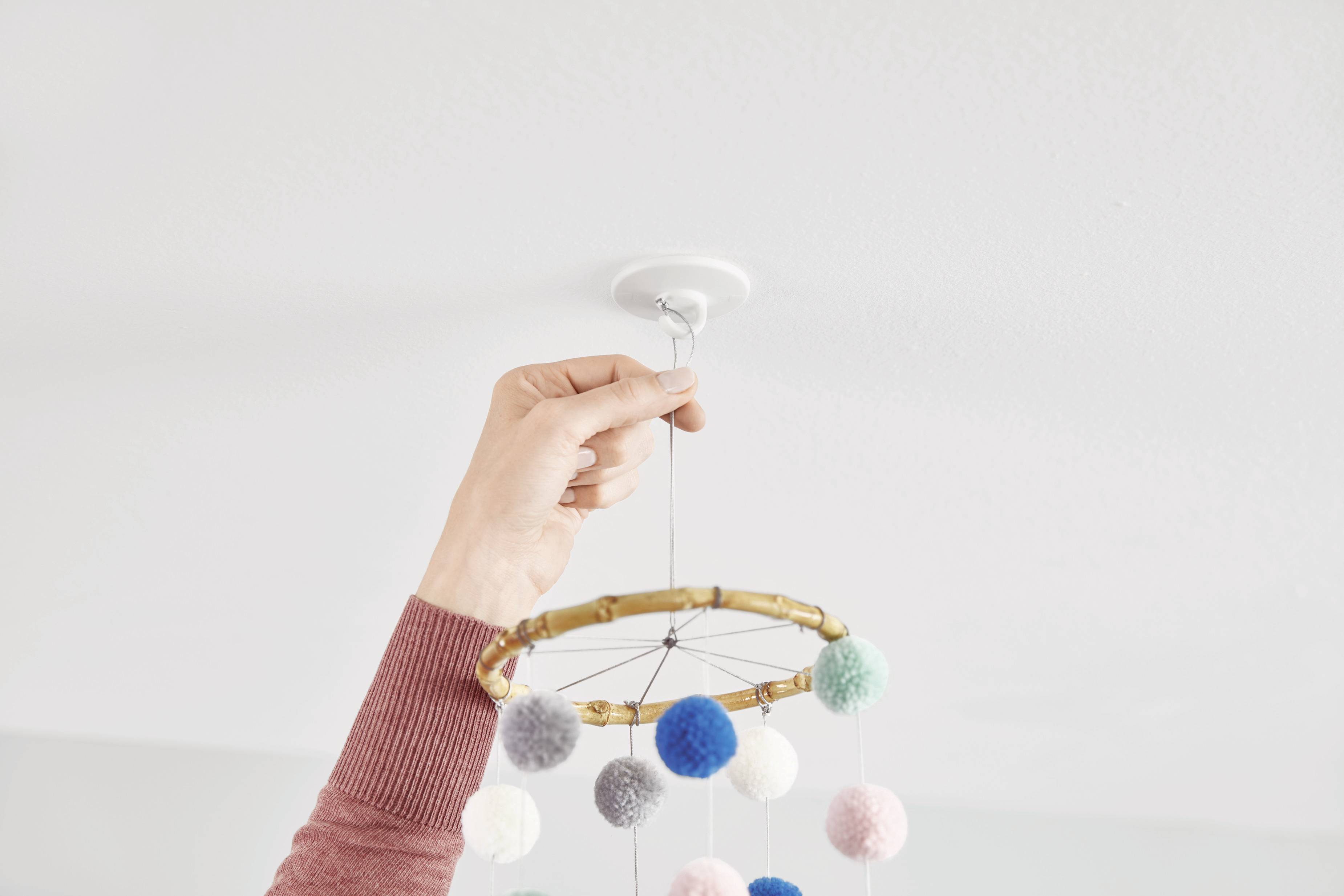 Une main fixe un mobile composé de boules de feutre colorées au plafond.