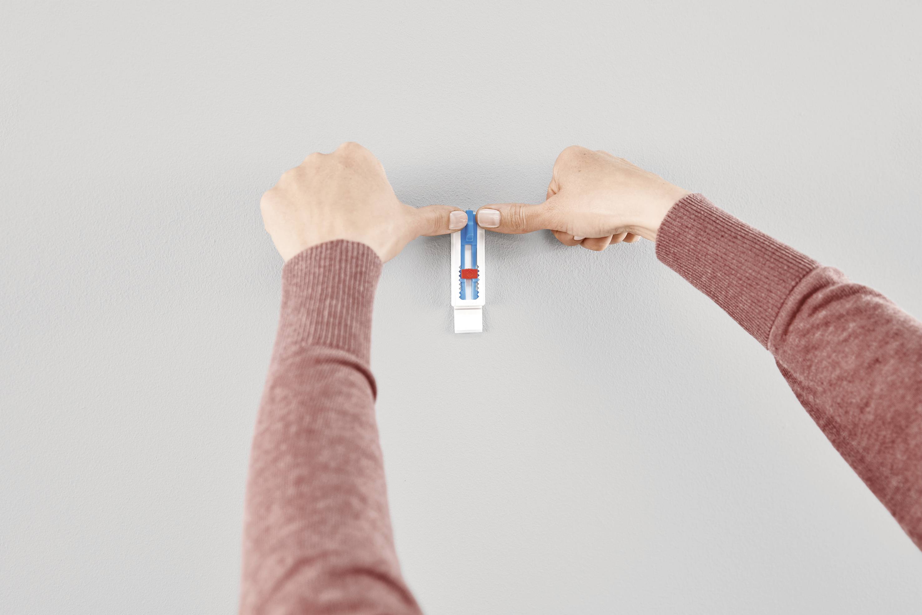 Deux mains accrochent une pince blanche avec un petit niveau à bulle sur un mur gris afin d'assurer un alignement précis.