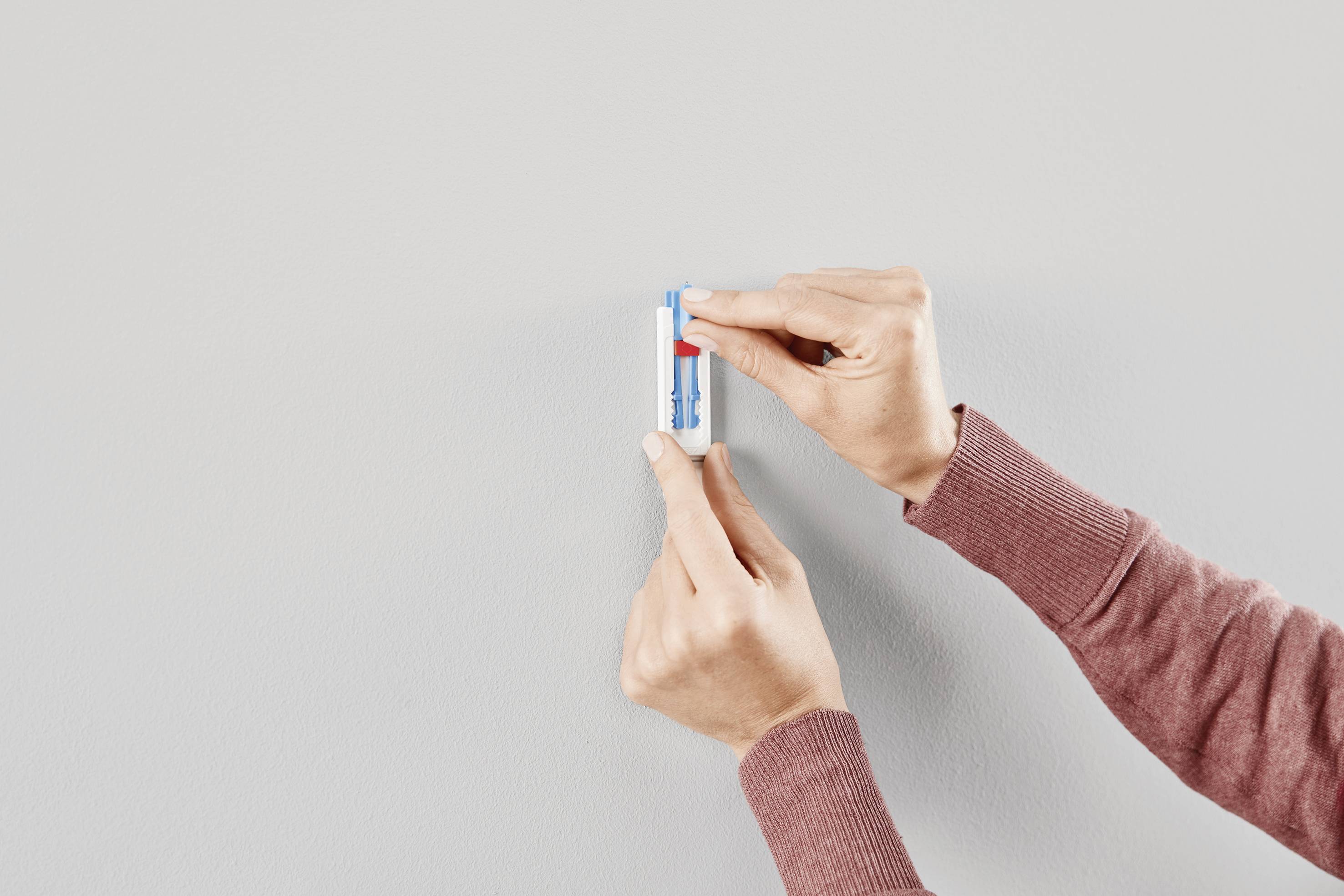Mains d'une personne tenant un baume à lèvres dans un étui bleu et blanc, sur un fond gris neutre.