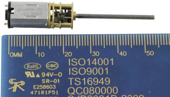 'Petit moteur électrique avec vis filetée, à côté d'une échelle bleue portant des certifications telles que ISO14001, ISO9001 et TS16949.'