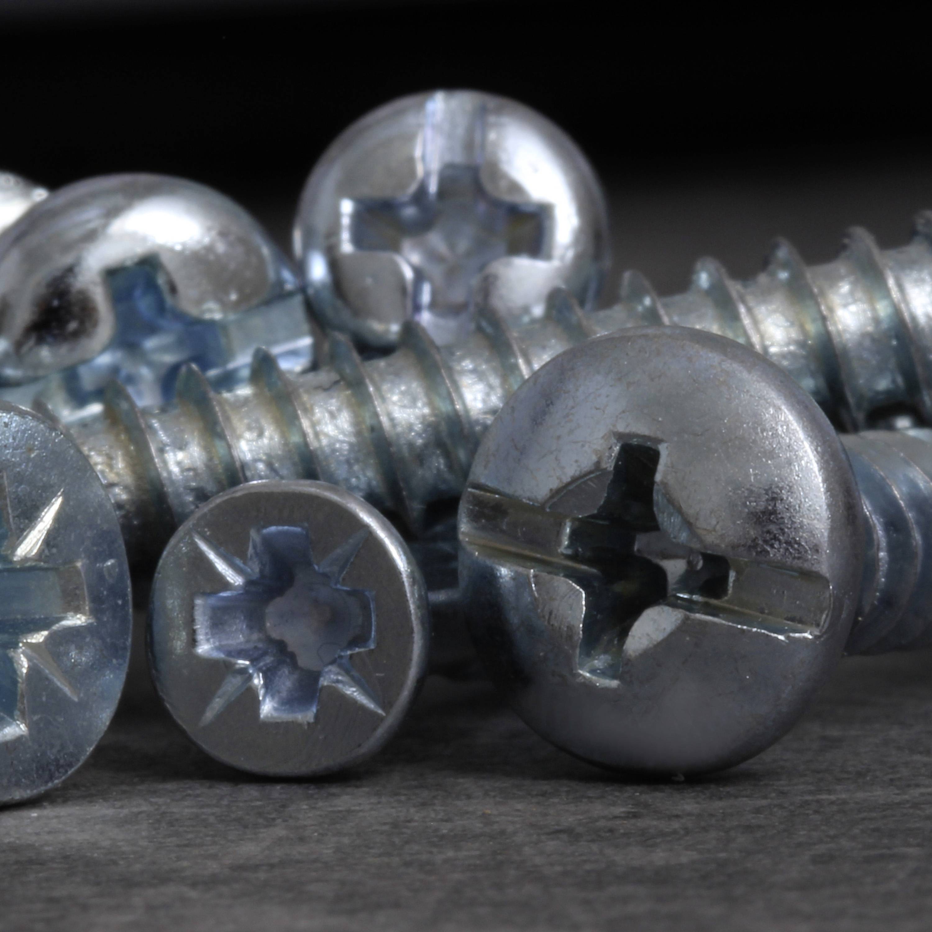 Plusieurs vis cruciformes en argent sont posées sur une surface grise.
