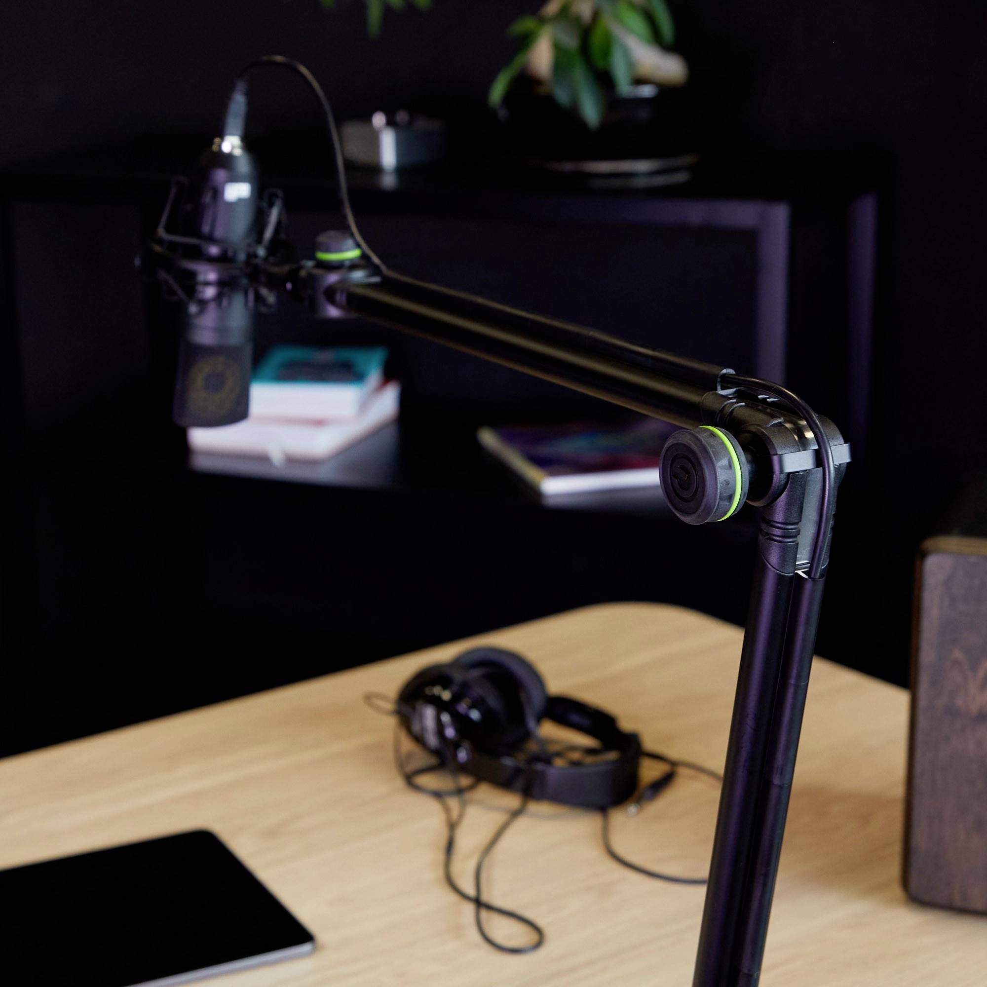 Un microphone sur un bras articulé au-dessus d'un bureau sur lequel sont posés des écouteurs, des livres et un ordinateur portable. Une plante se trouve en arrière-plan.