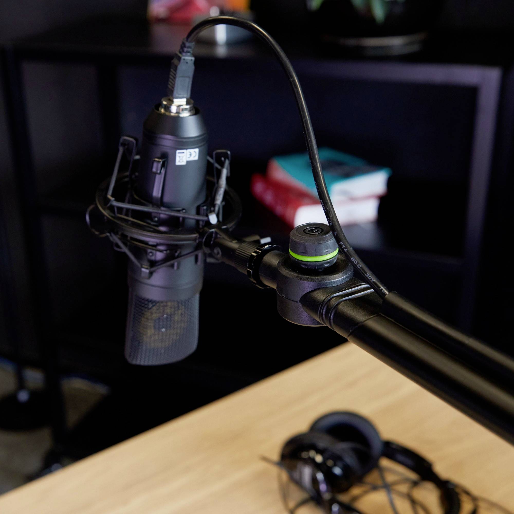 Un microphone posé sur une table illustre un environnement de podcast ou d'enregistrement. Des écouteurs sont posés à côté, avec des livres en arrière-plan.