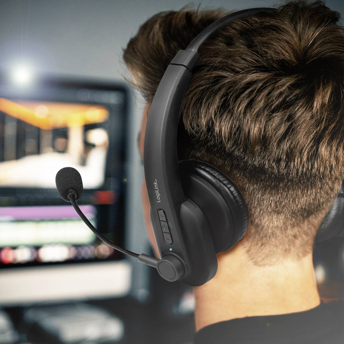 Un homme portant un casque travaille devant un écran d'ordinateur. L'accent est mis sur le casque, utilisé pour une communication professionnelle.