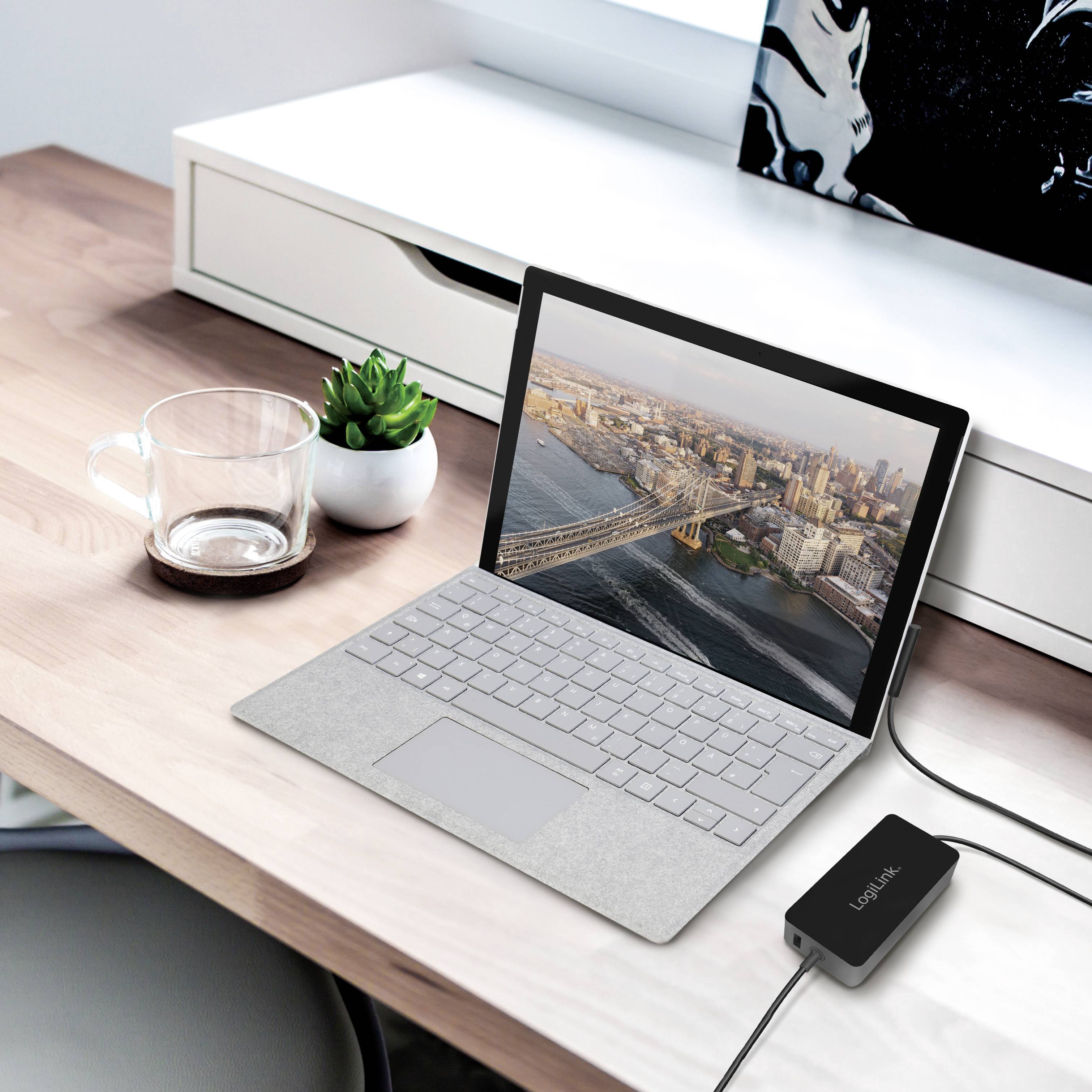 Un ordinateur portable sur un bureau affiche une image de paysage urbain. À côté se trouvent une tasse en verre vide et un appareil électronique.