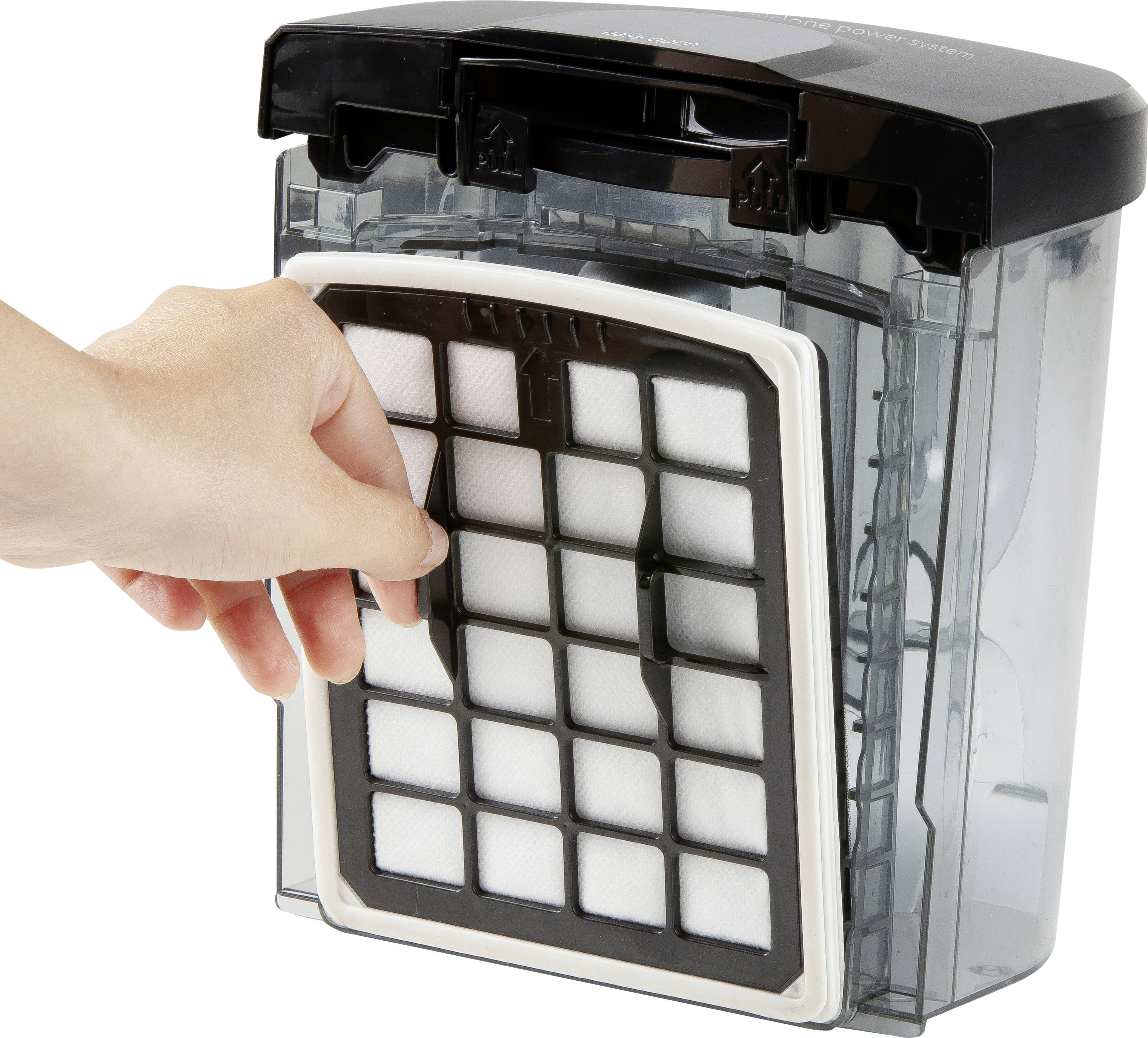 Une main retire le filtre d'un récipient rectangulaire et transparent d'aspirateur.