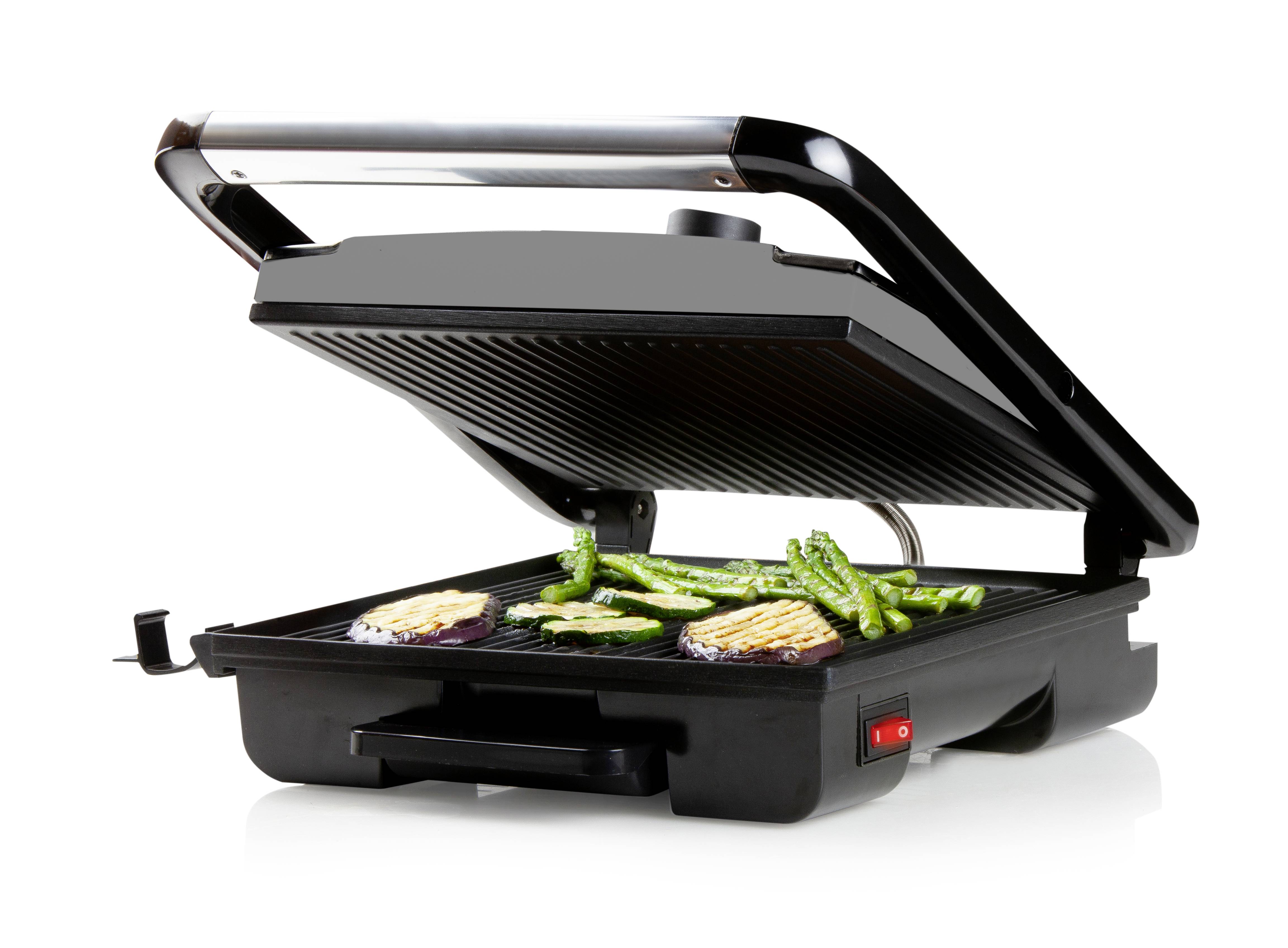 Grill électrique avec le couvercle ouvert. Sur la surface de cuisson, différents morceaux de légumes sont disposés, dont des asperges et des aubergines.