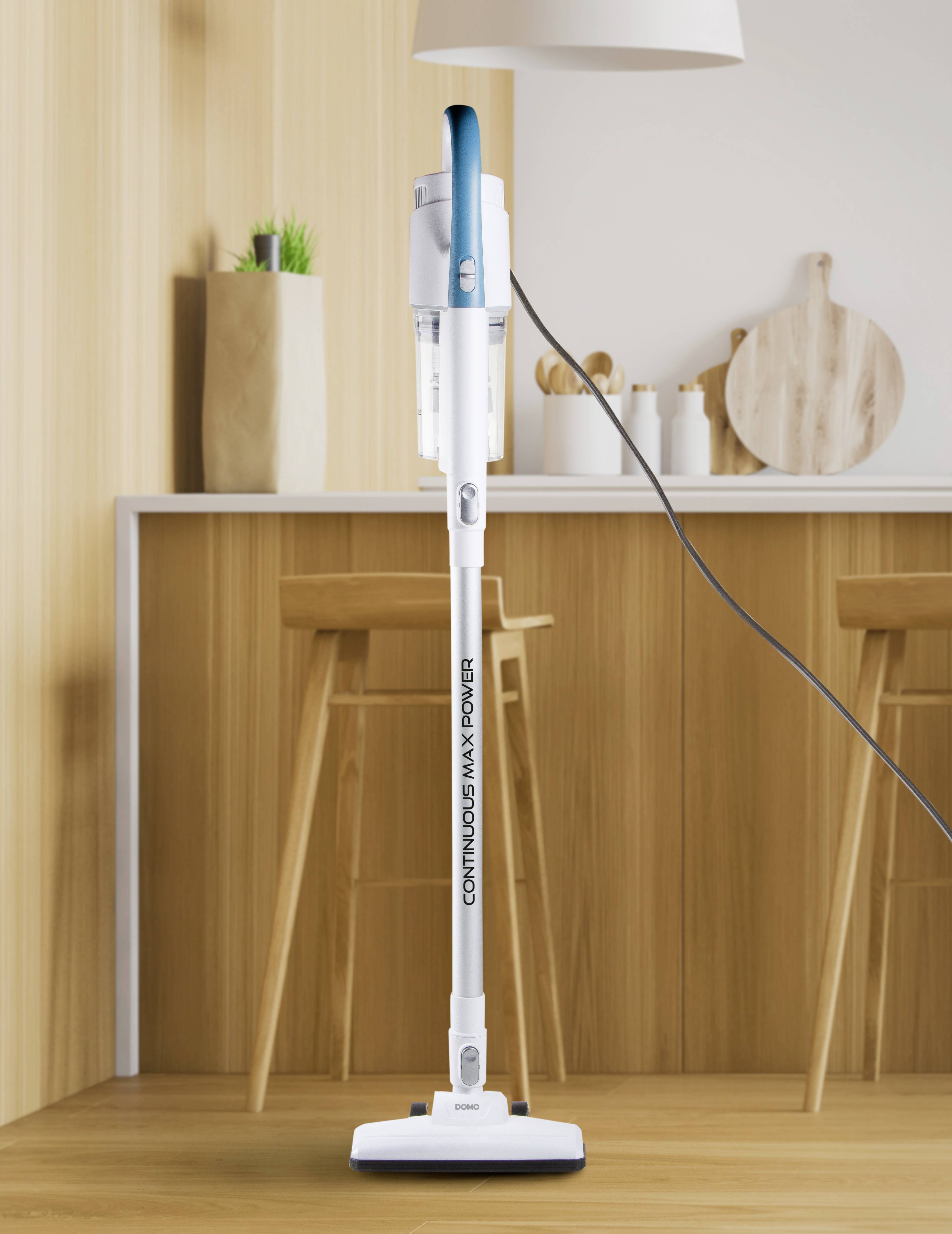 Un aspirateur blanc avec des touches bleues se trouve dans une cuisine moderne devant un comptoir de bar avec des tabourets de bar et des décorations en bois.