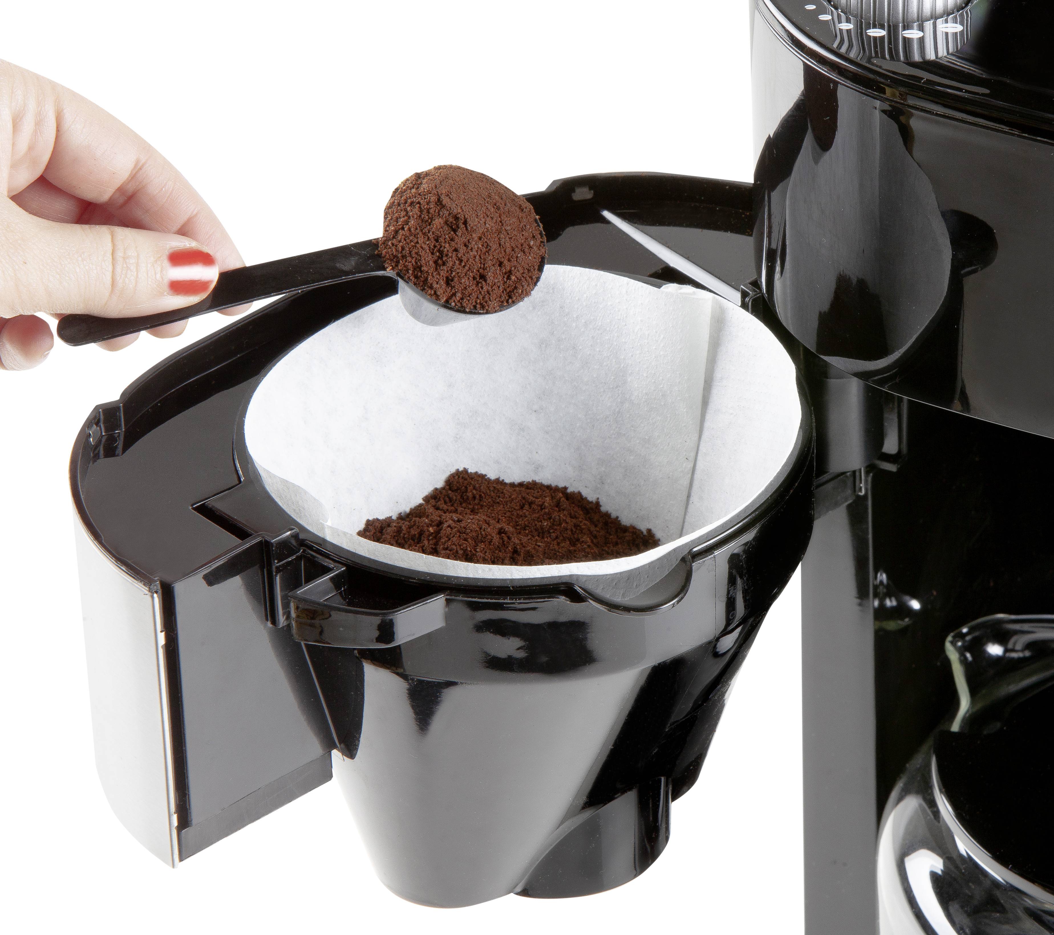 Une main remplit le filtre à café d'une machine à café avec une cuillère doseuse de café moulu.