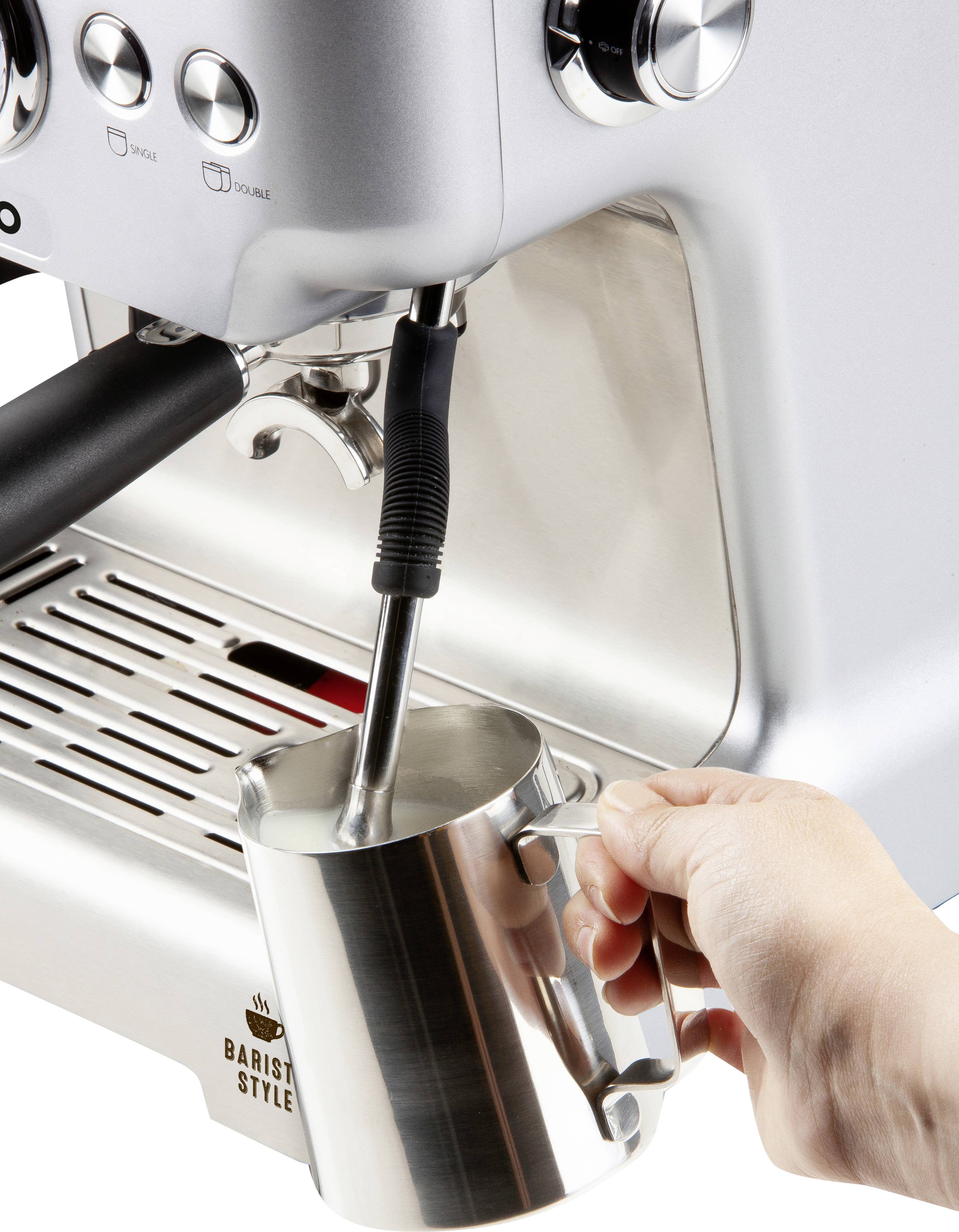 'Une main tient un pichet de lait sous le bec vapeur d'une machine à espresso pour faire mousser le lait.'