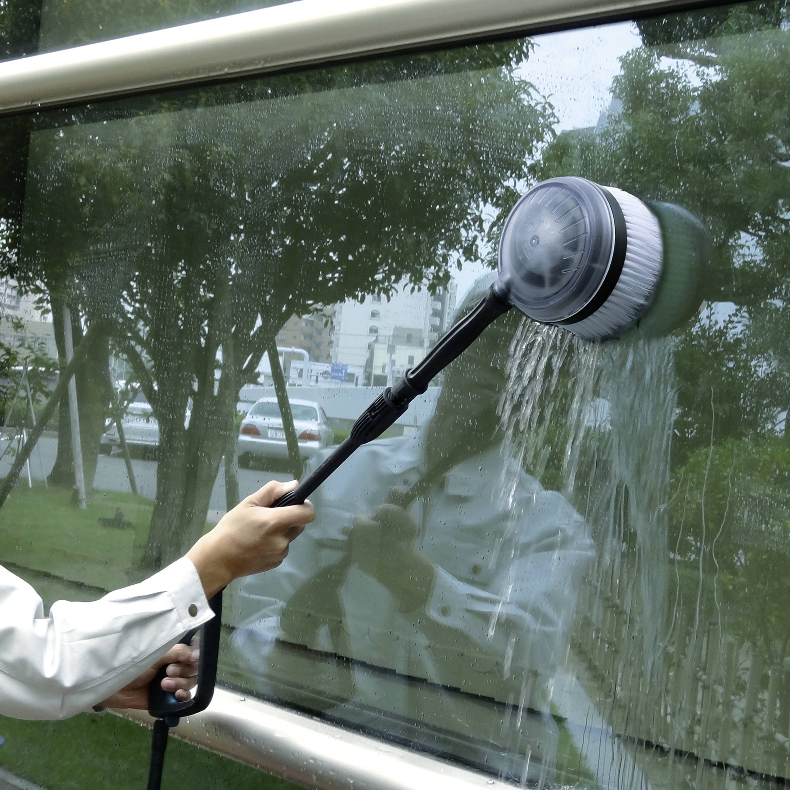 Une personne nettoie une fenêtre avec une brosse électrique ; l'arrière-plan montre un paysage urbain flou.