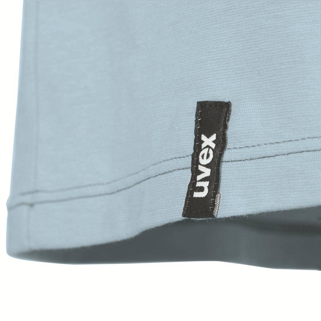 Pièce vestimentaire bleue avec l'étiquette 'uvex' visible en bas à droite de la couture.