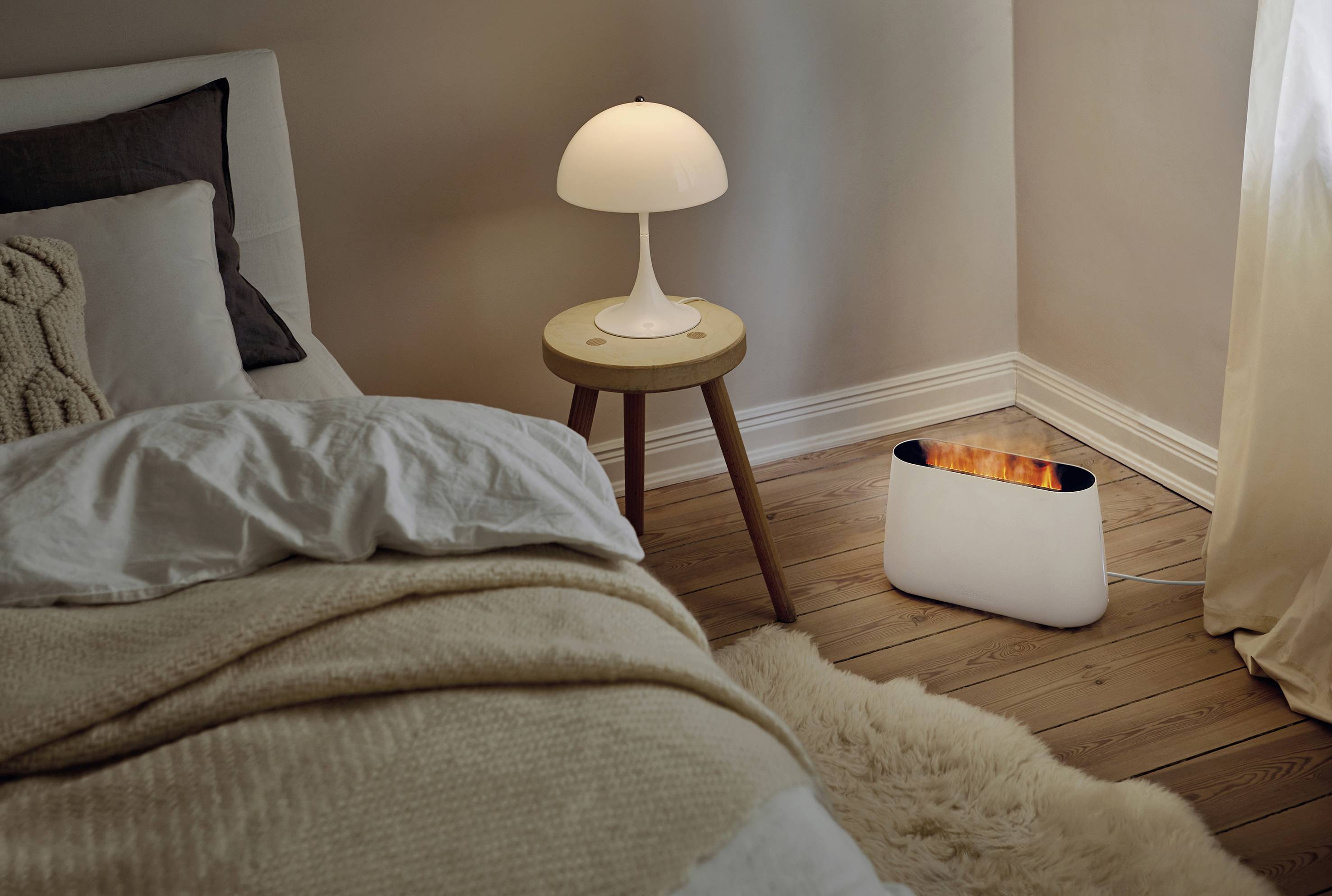 Une chambre confortable avec un lit, une table de chevet et une lampe. Sur le sol, un boîtier blanc est posé à côté du lit.