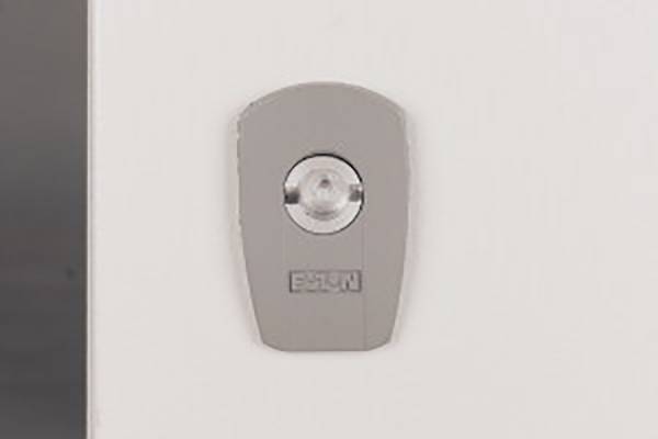 Un bouton d'ouverture de porte argenté est monté sur un mur blanc. Le bouton a un centre rond et transparent et est de la marque 'ESIN'.