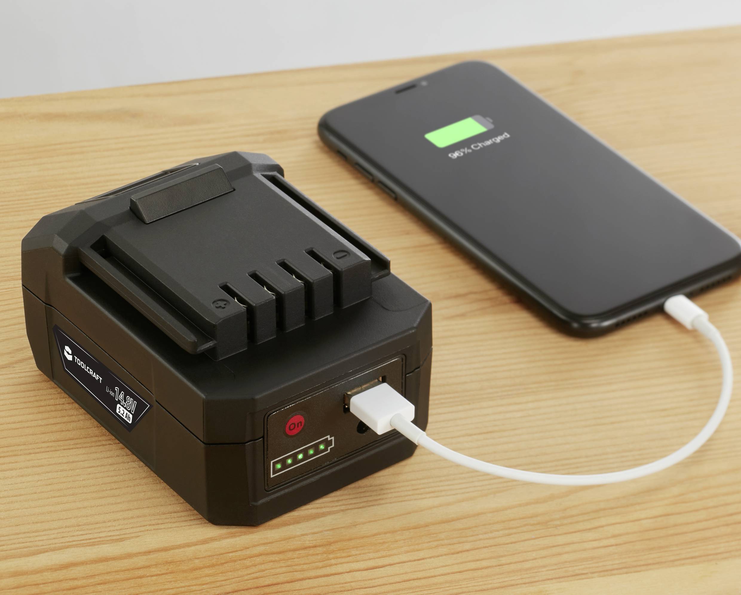 Un smartphone est en train d'être chargé avec un chargeur portable posé sur une table en bois. L'état de charge du téléphone est affiché.