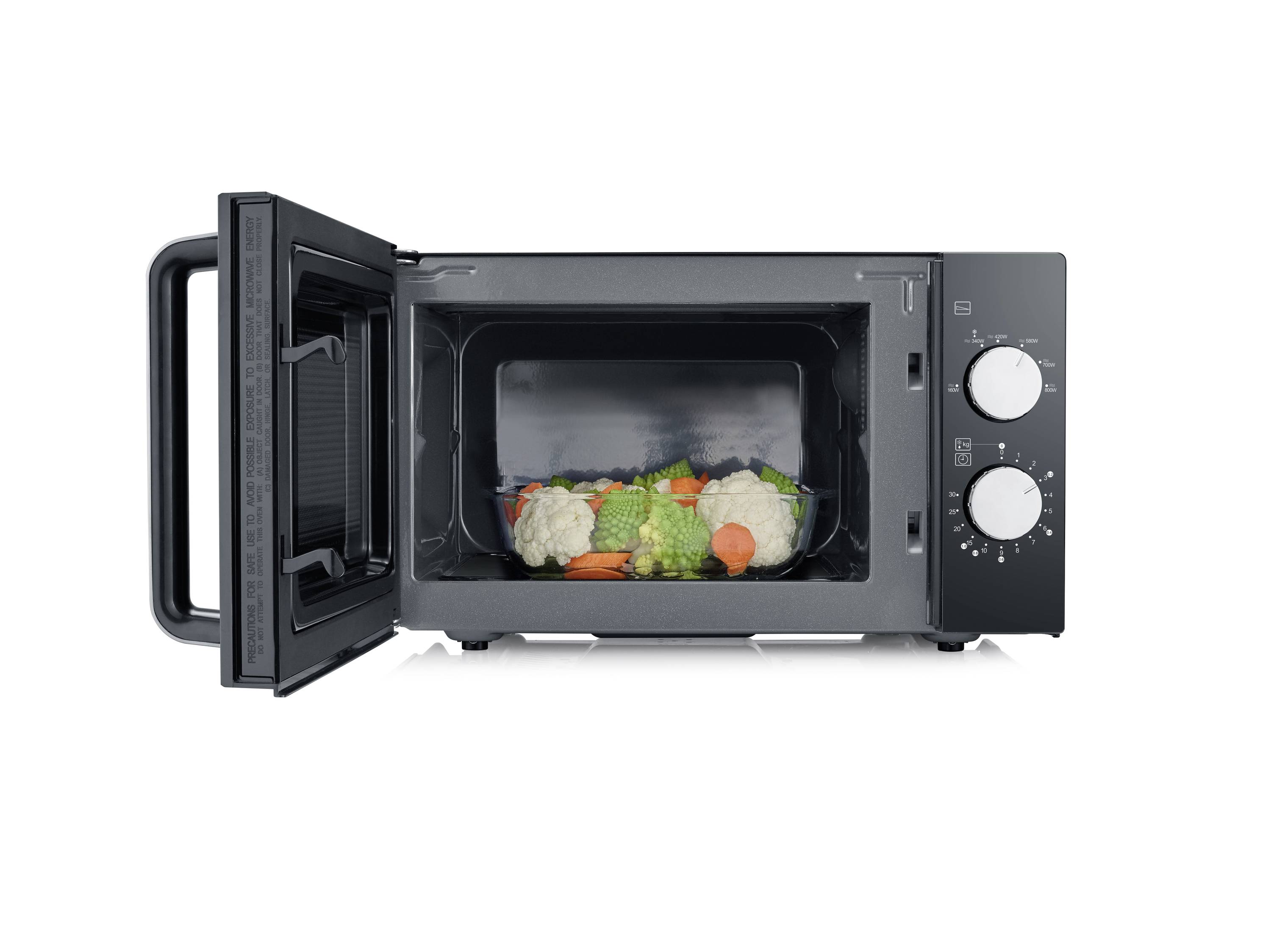 Four à micro-ondes ouvert avec une assiette remplie de légumes colorés tels que du brocoli, du chou-fleur et des carottes.