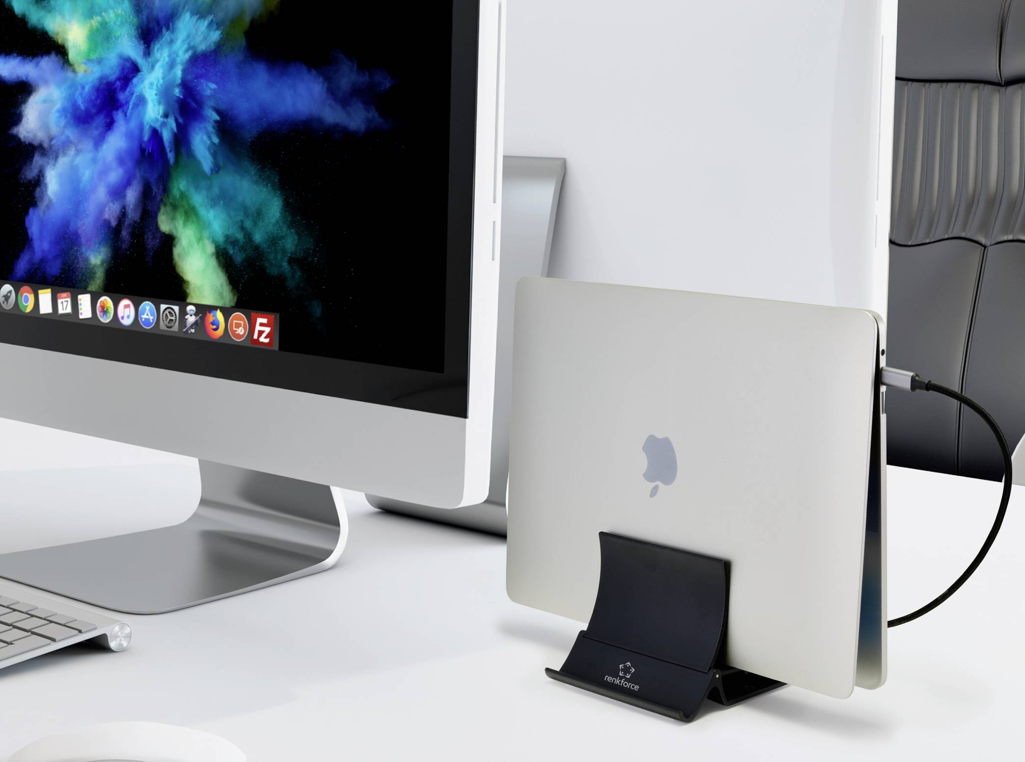 Un écran d'ordinateur affiche des nuages colorés. À côté, un ordinateur portable fermé est posé verticalement dans un support sur un bureau.