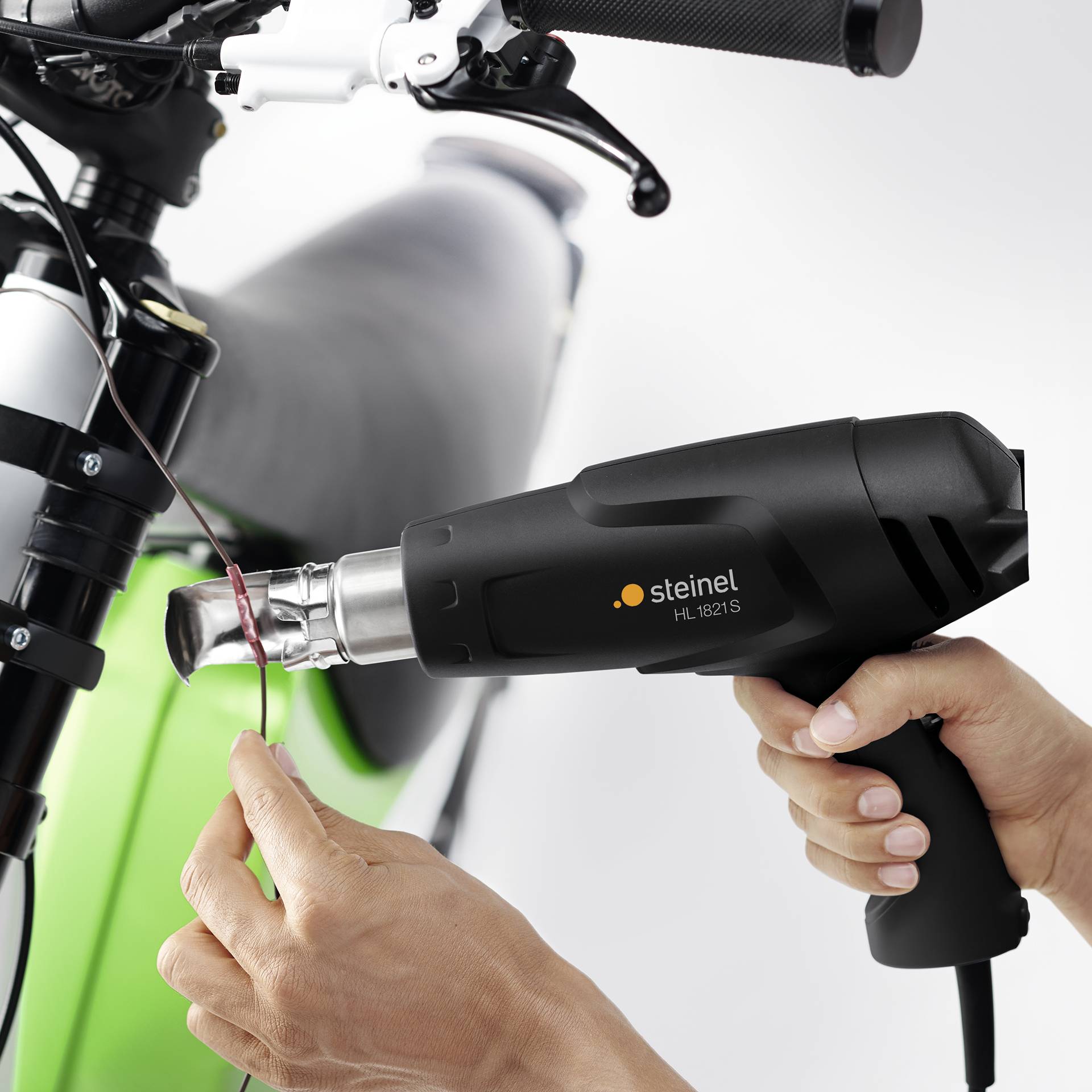 Une personne utilise un sèche-cheveux noir pour travailler un câble sur un guidon de vélo.