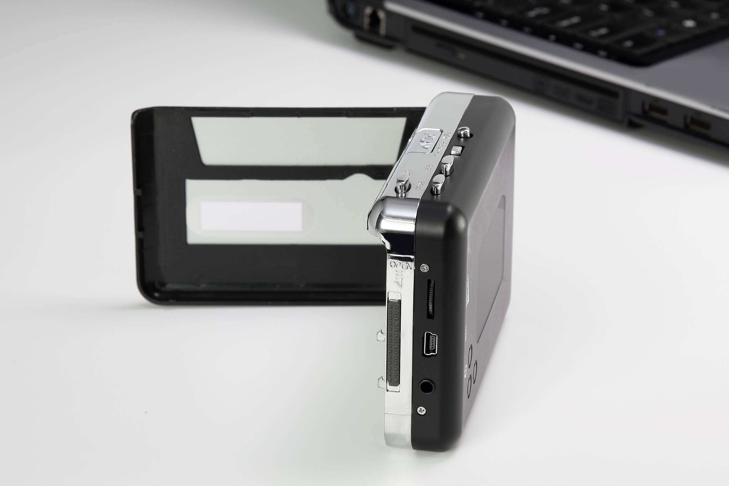 Appareil photo numérique avec écran rabattable, posé sur une table blanche à côté d'un clavier d'ordinateur portable ouvert.