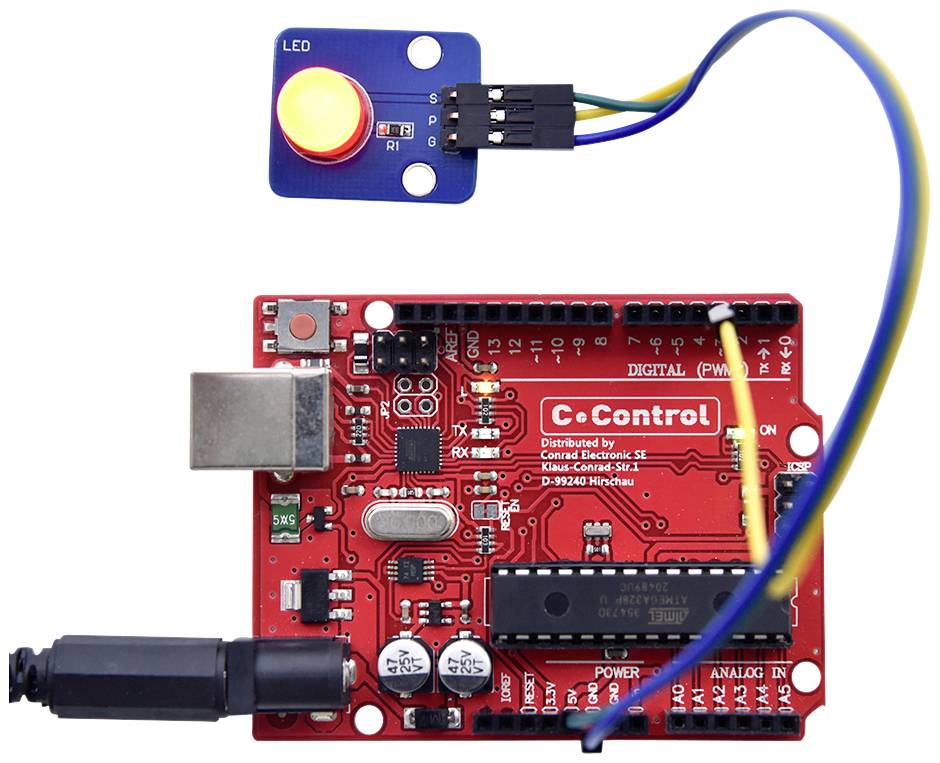 Une carte de microcontrôleur rouge connectée à des câbles, avec un capteur bleu qui contient une LED rouge et un bouton jaune.