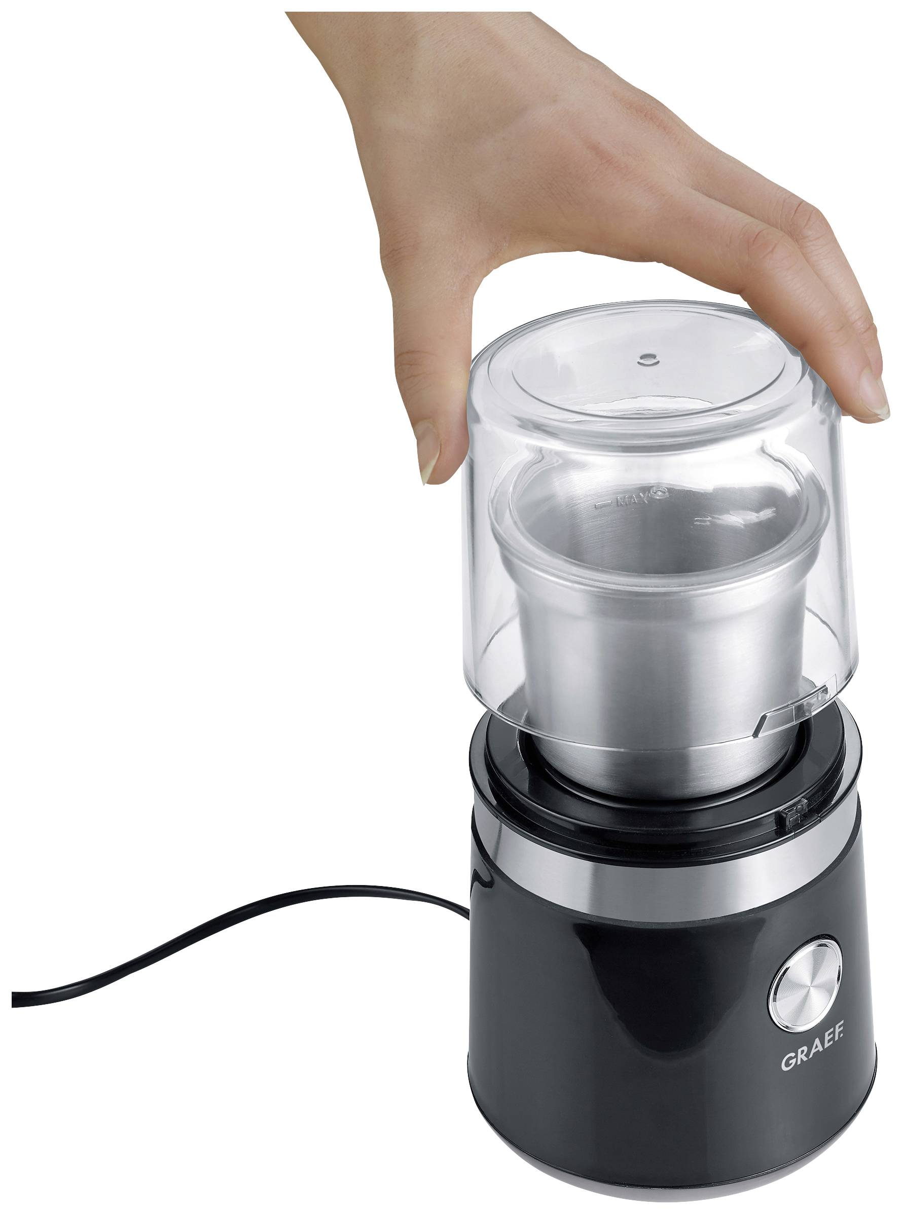 Une main actionne un moulin à café électrique noir avec un couvercle transparent sur un fond blanc.