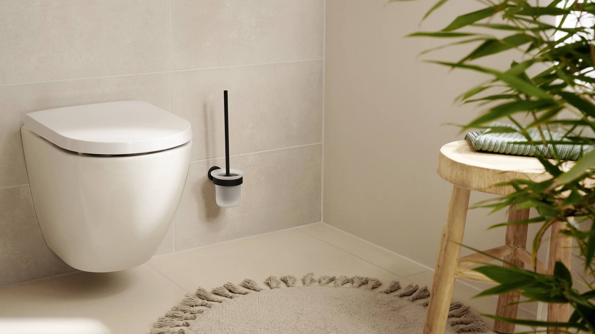 Une salle de bain moderne avec des toilettes murales blanches, une brosse de toilette à côté, un tabouret en bois et un arrangement de plantes.