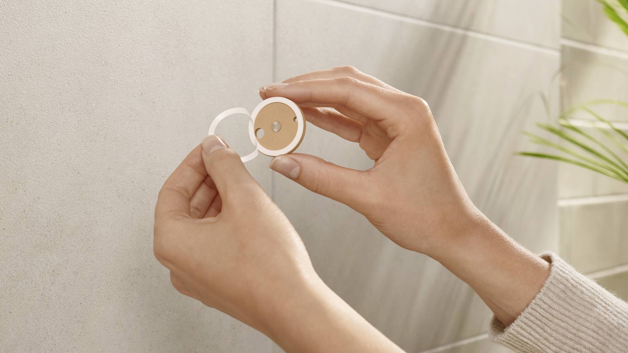 Une personne tient un support magnétique rond et blanc devant un mur. Le support présente une surface beige et semble petit et compact.