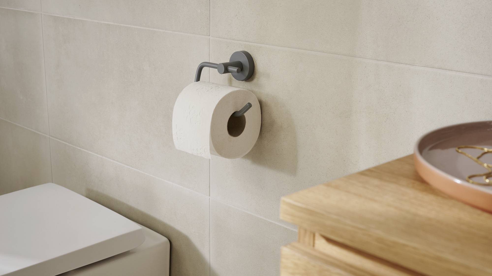 Rouleau de papier toilette sur son support mural dans une salle de bain, à côté d'un siège de toilettes blanc et d'une étagère en bois décorée.