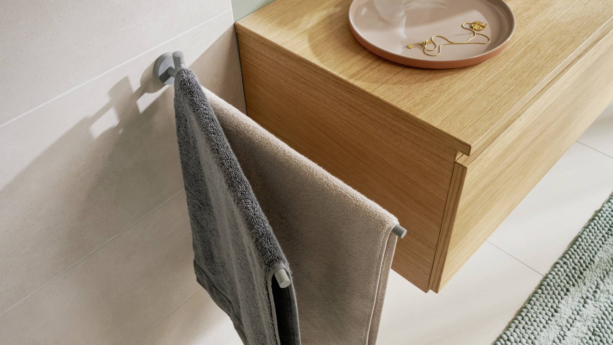 L'image montre une salle de bain moderne avec un porte-serviettes mural sur lequel sont suspendus deux serviettes, et une étagère en bois portant un plateau.