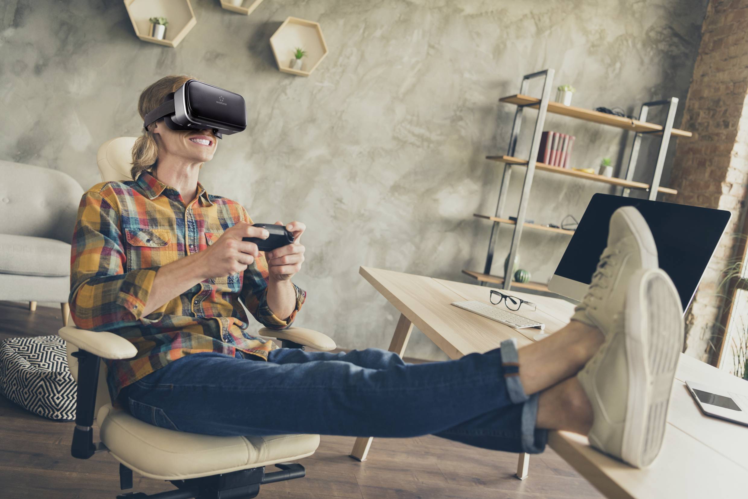 Une personne est assise de manière détendue, les pieds sur la table, portant un casque de réalité virtuelle et tenant une manette de jeu.