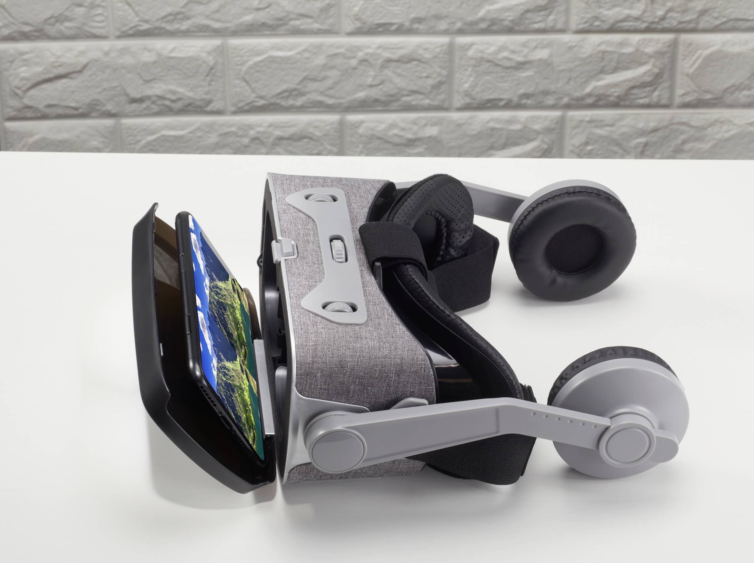 Lunettes de réalité virtuelle posées sur une table, avec un smartphone servant d'écran. Arrière-plan en motif de briques grises.