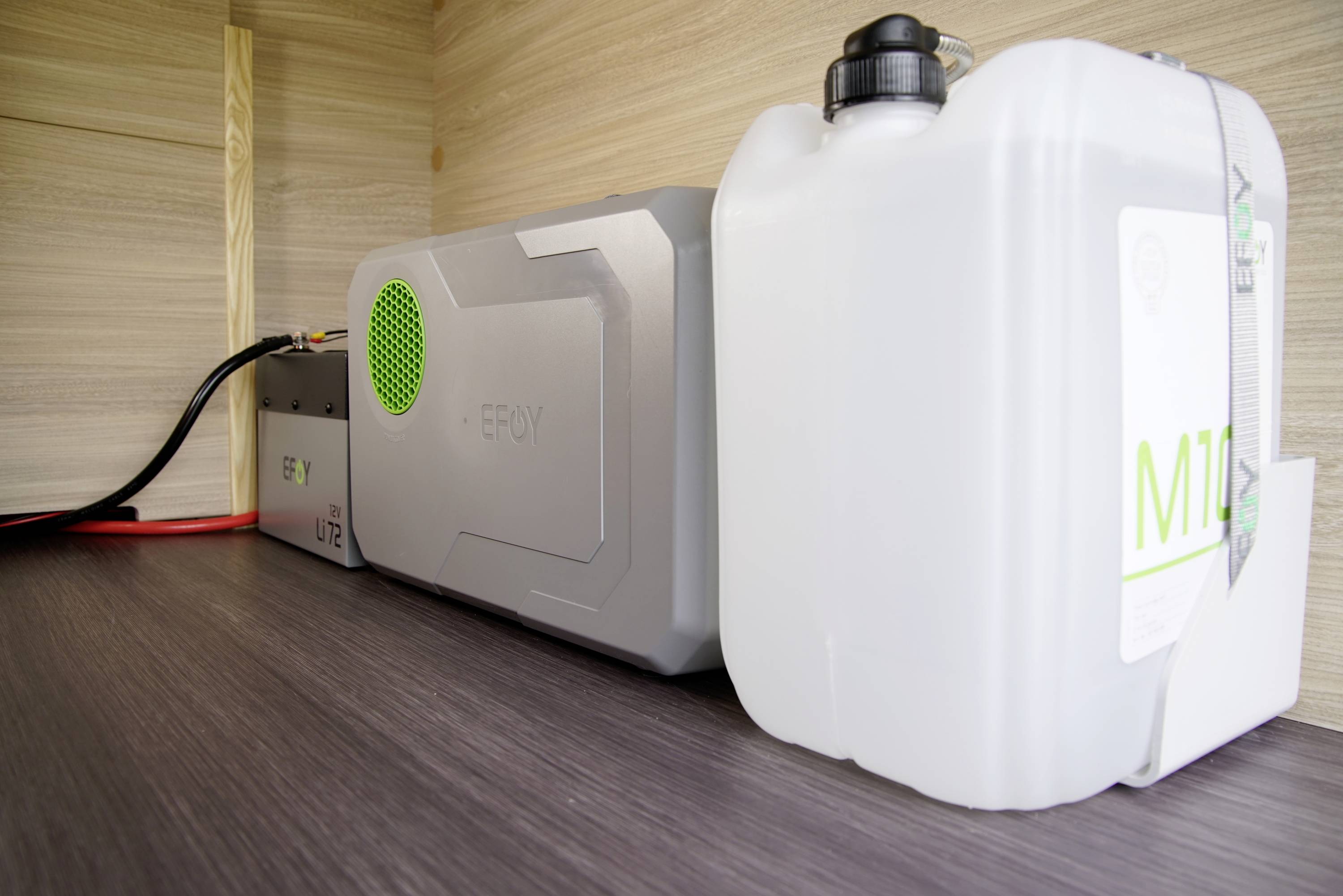 Un dispositif de stockage d'énergie gris avec un ventilateur vert et un bidon en plastique blanc sont posés sur une surface en bois.