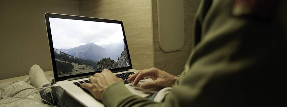 Une personne tape sur un ordinateur portable dont l'écran affiche un paysage de montagne. L'ordinateur portable est posé sur une table.
