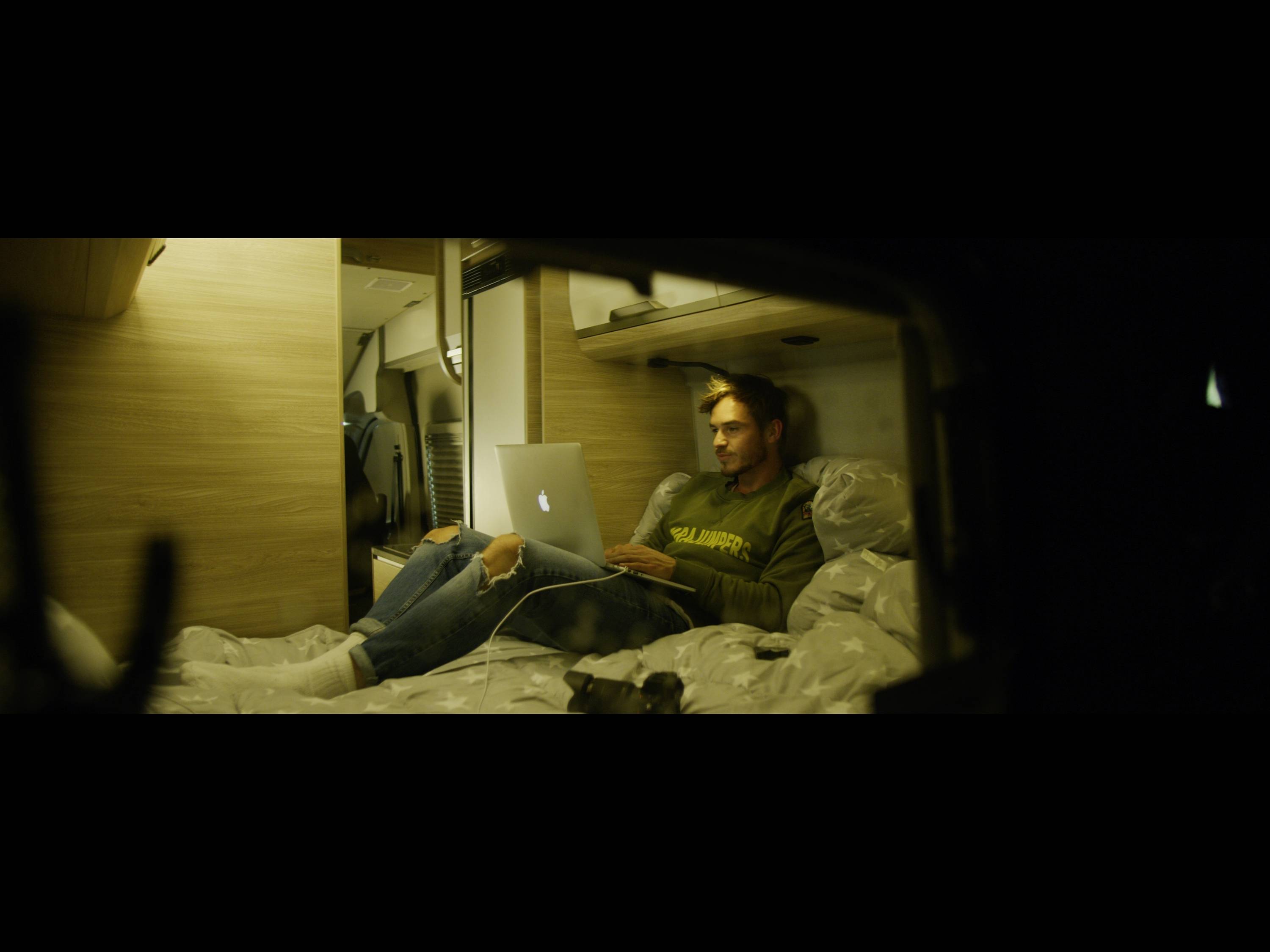 Une personne est assise confortablement sur un lit dans un camping-car et travaille sur un ordinateur portable.