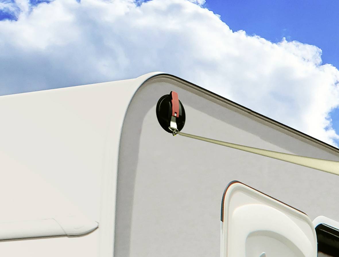 Vue latérale d'une caravane avec une fenêtre de toit ouverte, devant un ciel bleu parsemé de nuages.