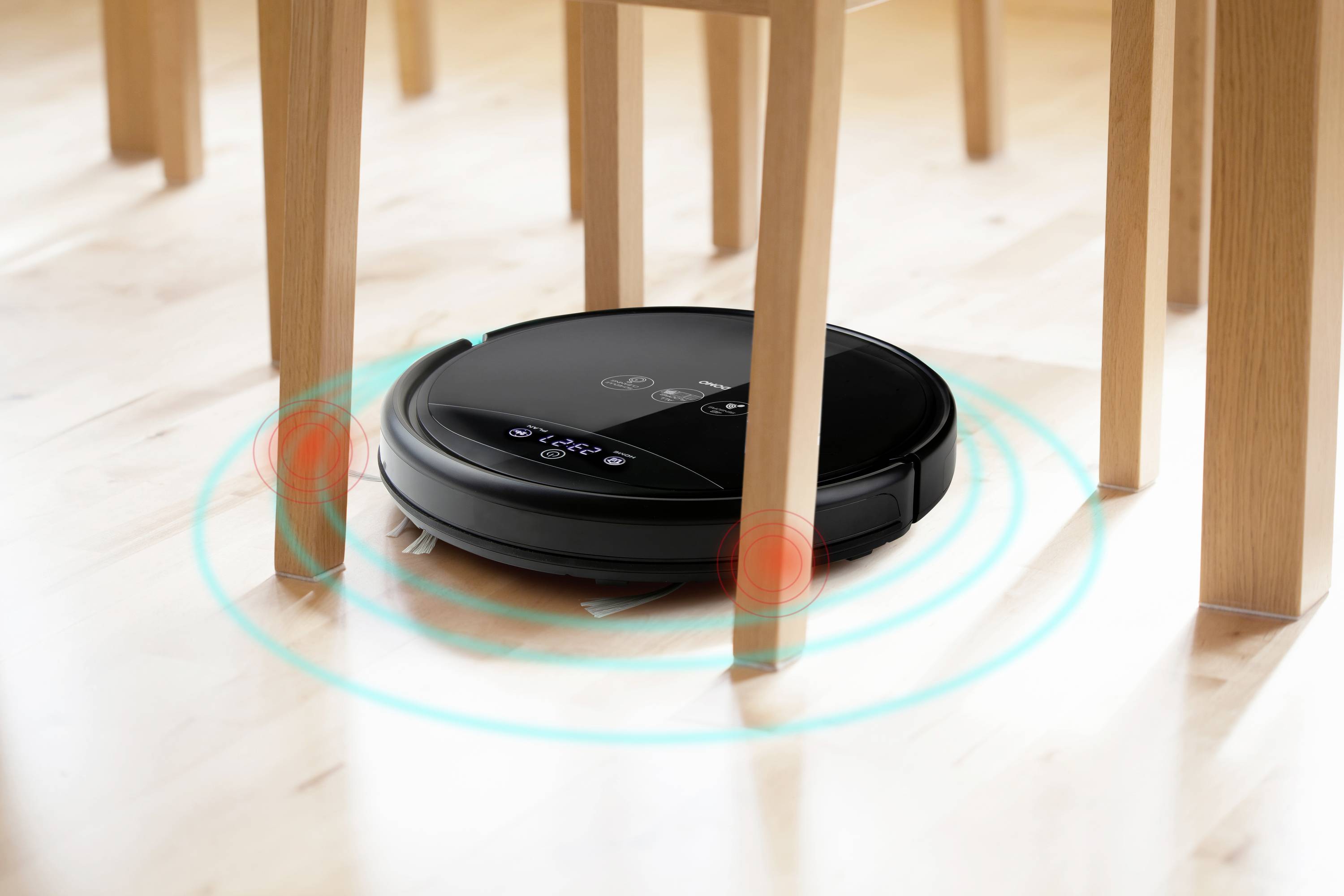 Un robot aspirateur navigue entre les pieds de chaises sur un parquet. Des anneaux lumineux bleus indiquent la présence de capteurs de détection d'obstacles.