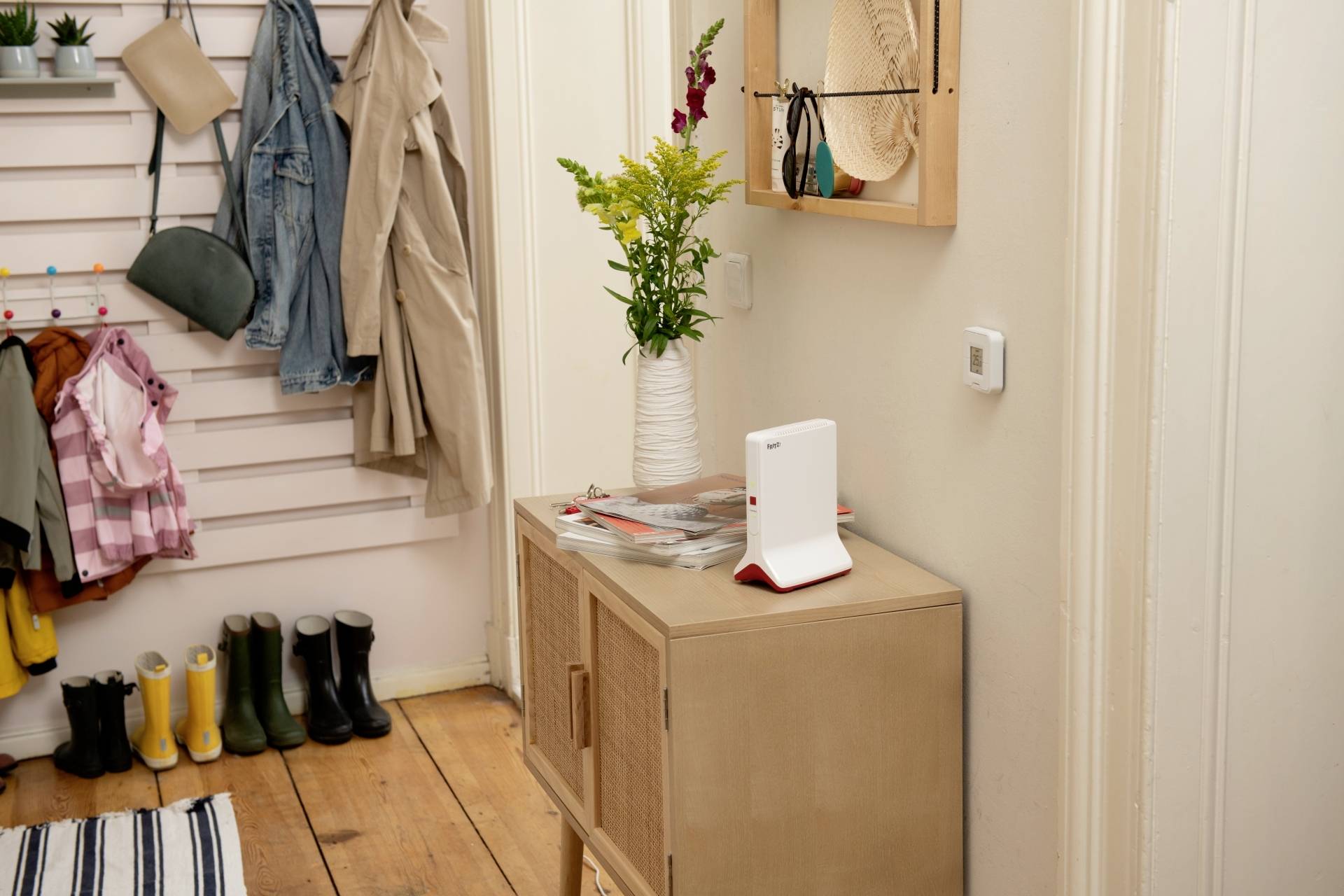 Entrée avec des chaussures, des vestes suspendues, une table avec des magazines et un vase de fleurs.