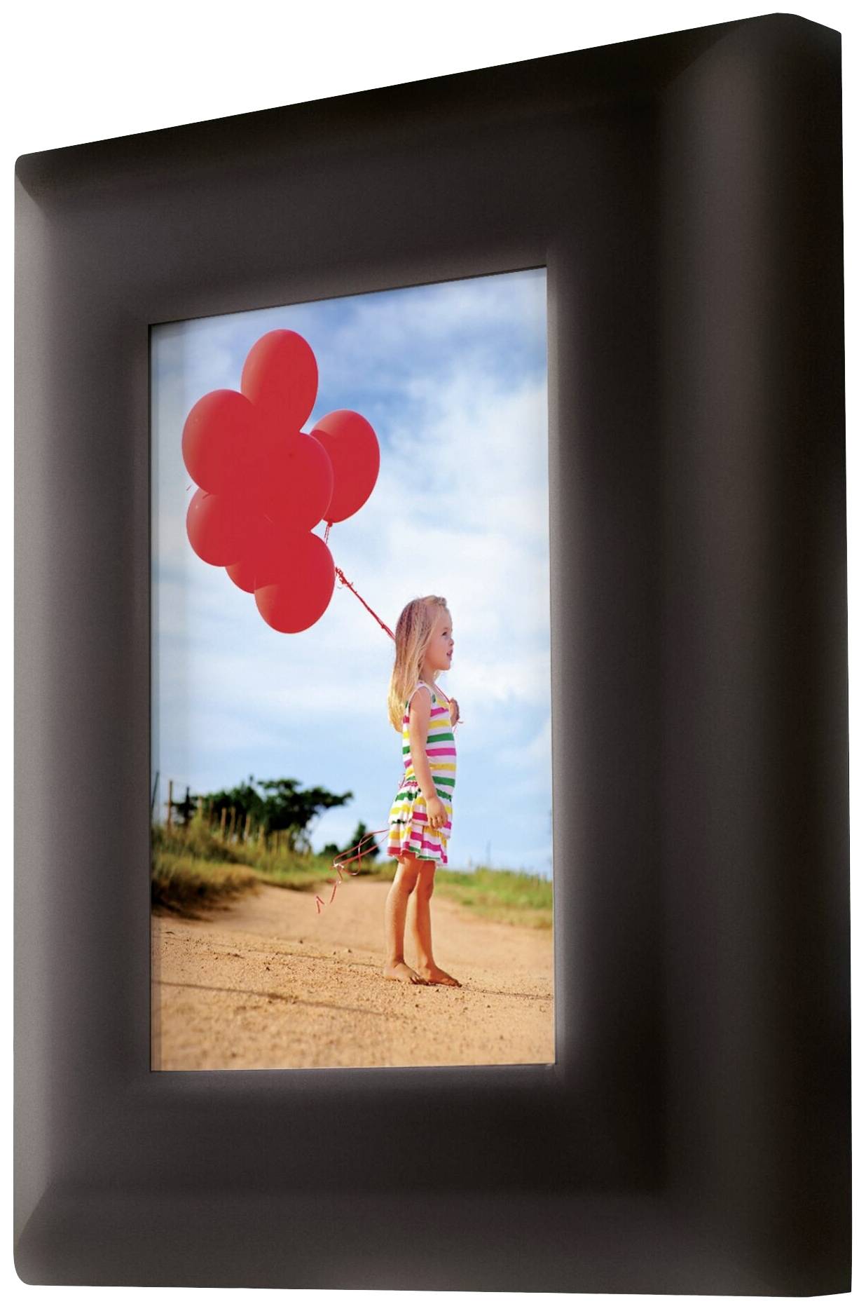 Une petite fille portant une robe rayée tient des ballons rouges. Elle se tient sur un chemin sablonneux sous un ciel bleu.