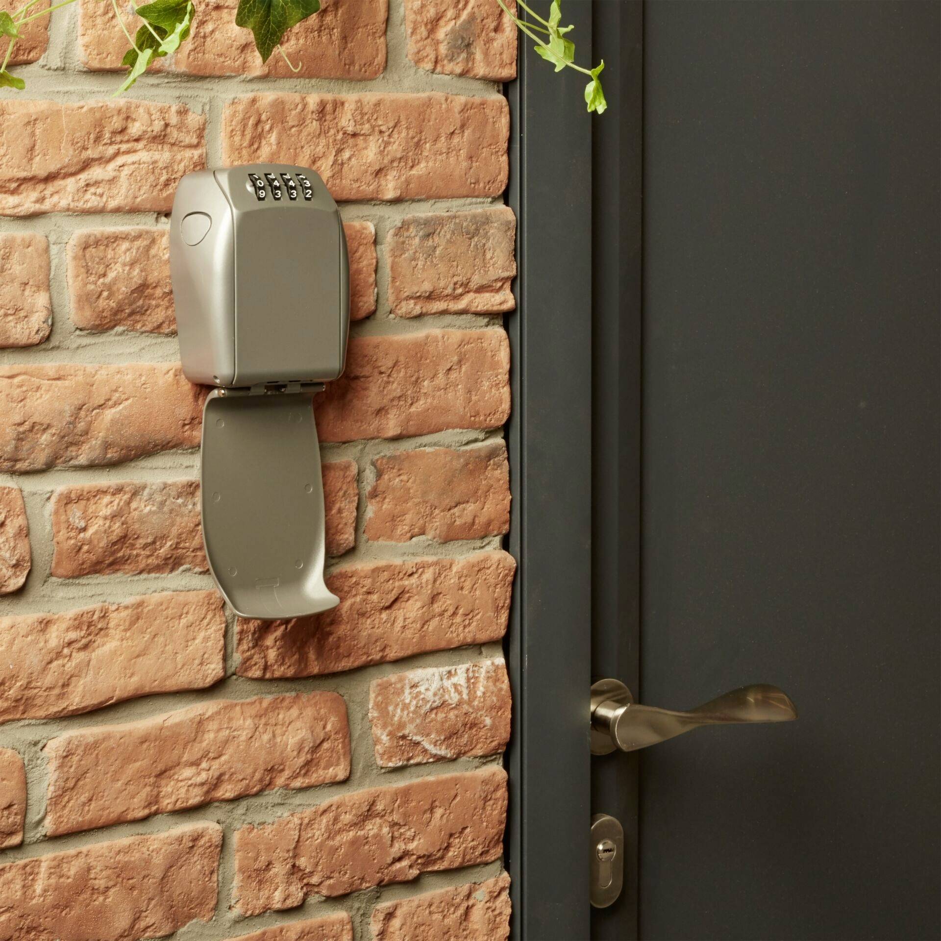 Un coffre-fort à clés fixé à un mur de briques à côté d'une porte fermée. Le coffre-fort est équipé d'un cadenas à combinaison pour le rangement sécurisé des clés.