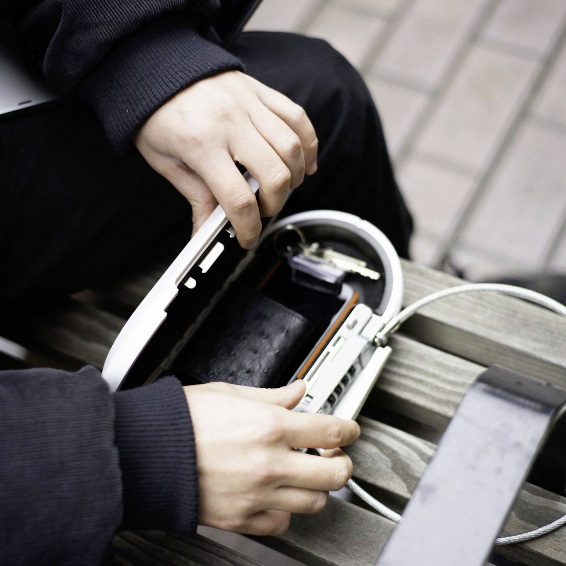 Une personne ouvre un étui de protection blanc sur un banc pour charger un smartphone. Un câble de charge est branché.